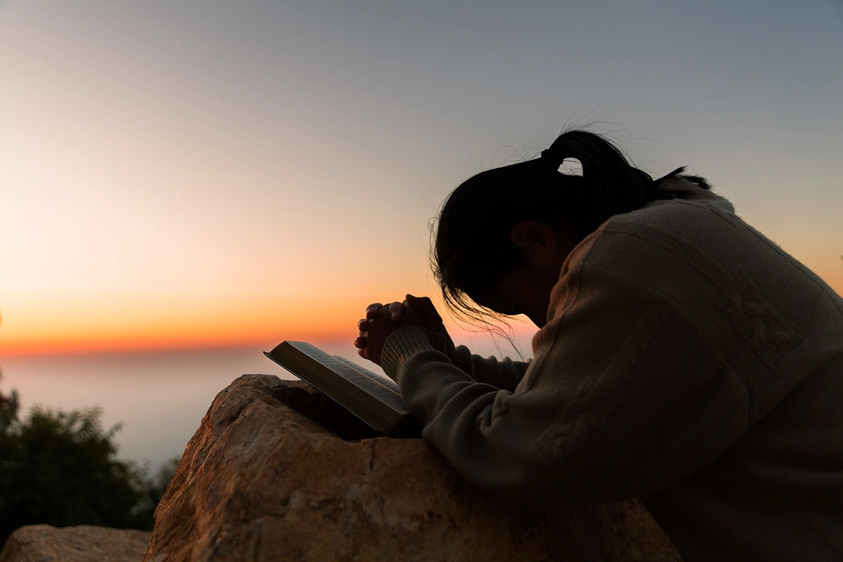Woman praying on a rock by the ocean.