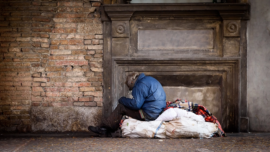 Elderly homeless person sitting on the street wrapped in blankets, illustrating the need for local church compassion initiatives through CityServe to help the hurting.