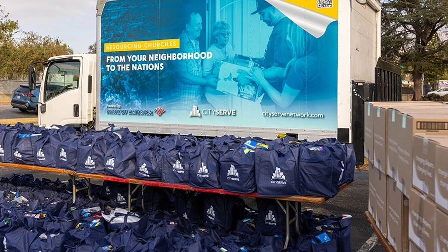 CityServe delivery truck and tables filled with navy blue bags ready for distribution, representing the GIK supply chain delivering goods to church PODs serving families in need.