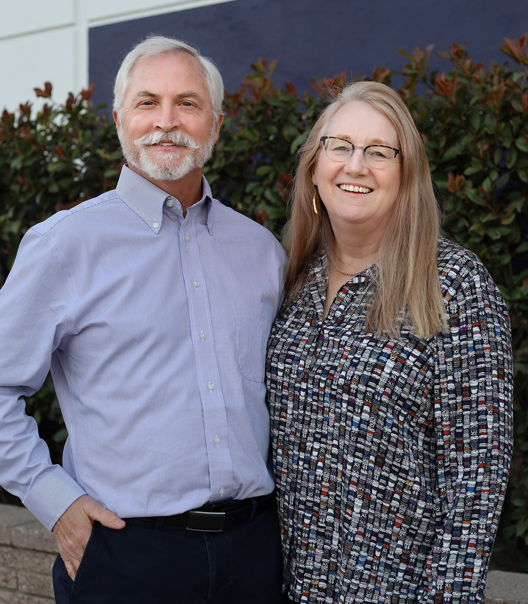 Burl and Theresa Evans, CityServe board members, smiling outside near greenery.