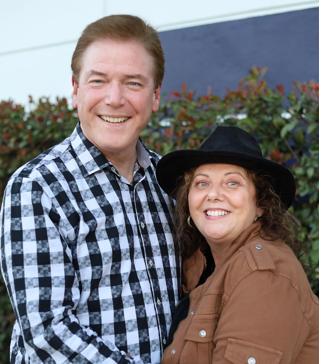 Scott and Darla Young, smiling outside in front of a green hedge, members of the CityServe board.